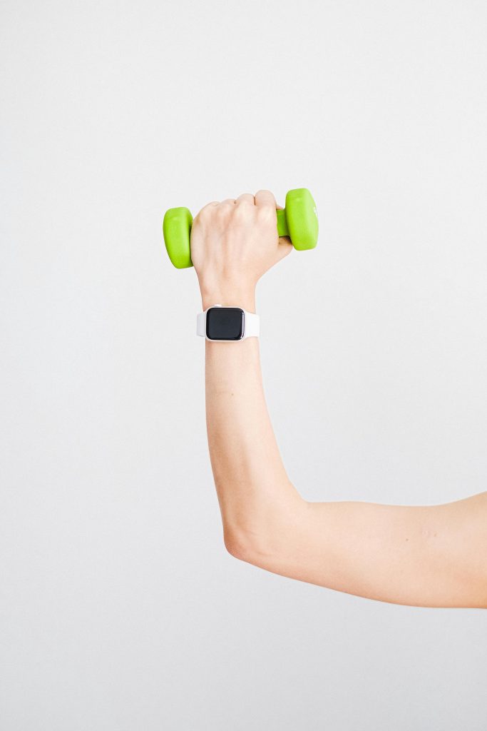 Arm holding a green dumbbell with a smartwatch on wrist against a white background.